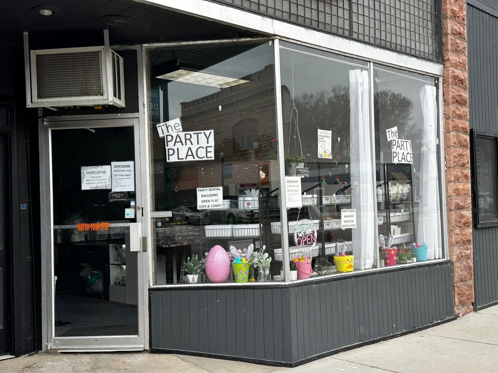 The Party Place storefront in downtown Dell Rapids, with display windows, an open sign, and signs listing party rental, balloons, open play, toys and candy